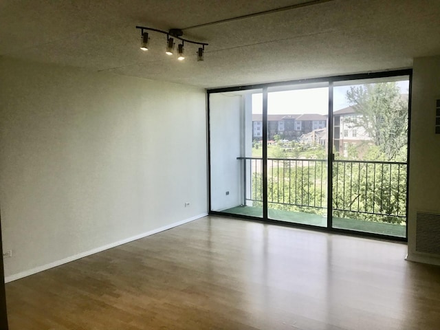 spare room with floor to ceiling windows, rail lighting, a textured ceiling, and hardwood / wood-style flooring