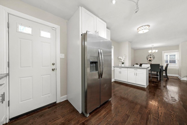 kitchen featuring light stone countertops, dark hardwood / wood-style floors, hanging light fixtures, stainless steel fridge, and white cabinetry