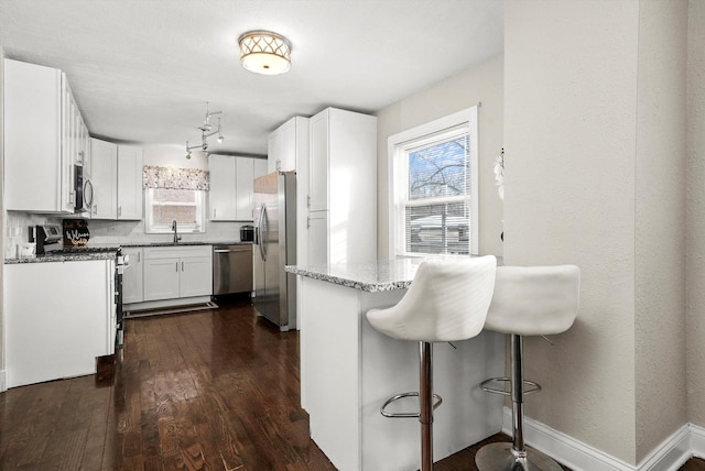 kitchen with appliances with stainless steel finishes, light stone counters, white cabinets, backsplash, and sink