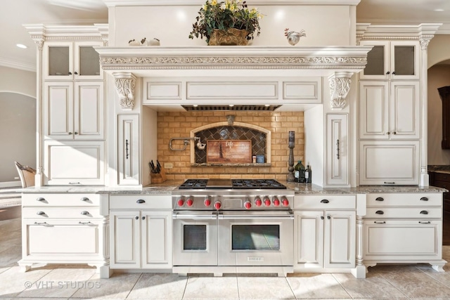 kitchen featuring light stone countertops, arched walkways, double oven range, ornamental molding, and glass insert cabinets