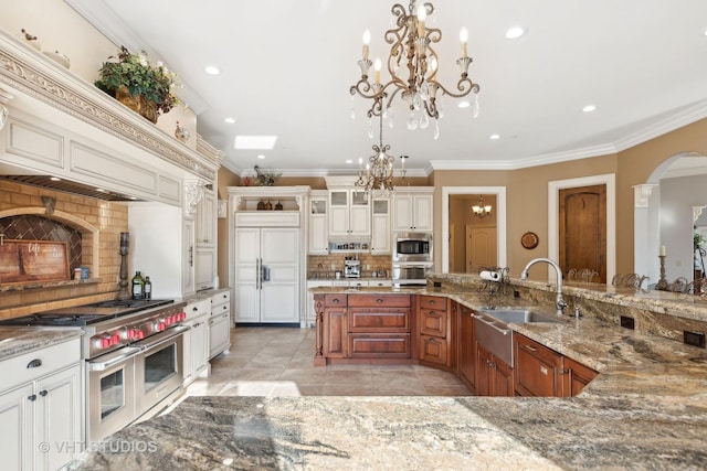 kitchen with arched walkways, tasteful backsplash, a sink, an inviting chandelier, and built in appliances