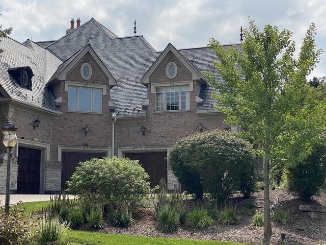 french provincial home with a high end roof, a chimney, and brick siding