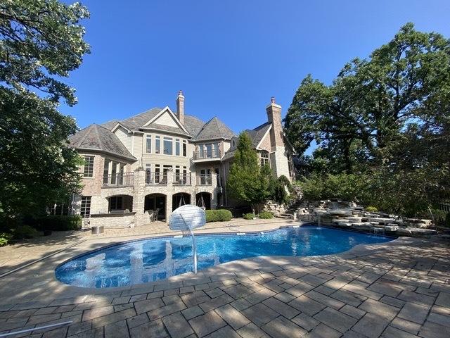 back of property with a patio, an outdoor pool, stone siding, and a balcony