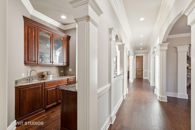 hallway with arched walkways, ornamental molding, dark wood-style floors, and ornate columns