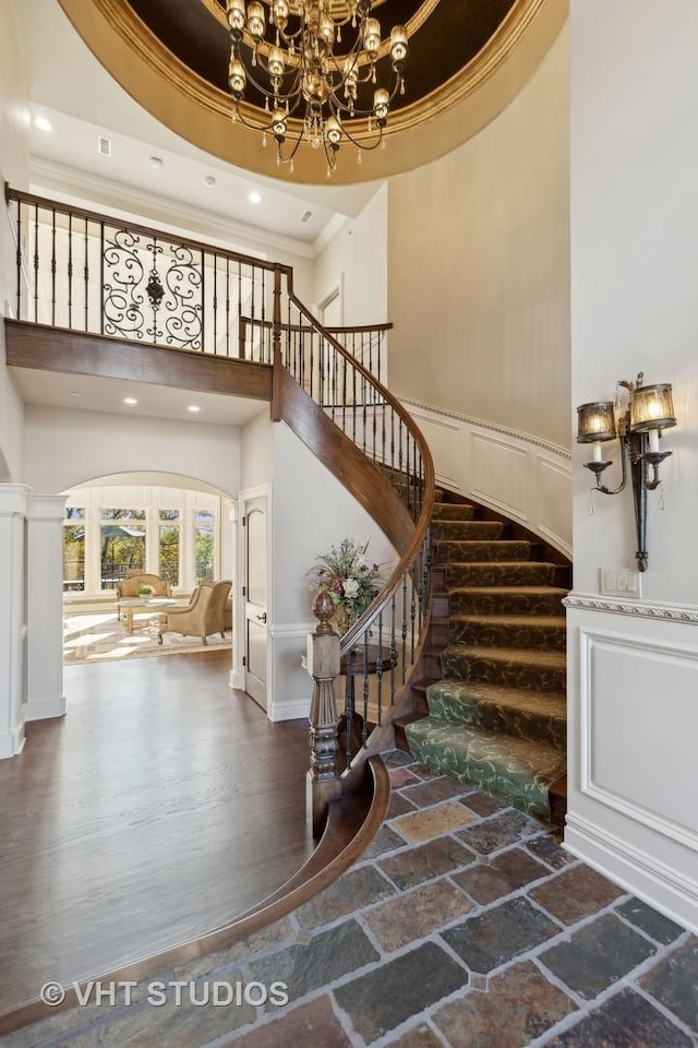 staircase featuring a high ceiling, an inviting chandelier, recessed lighting, ornamental molding, and stone tile flooring