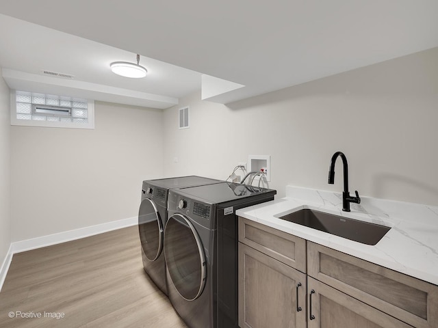 laundry room with sink, washing machine and dryer, light wood-type flooring, and cabinets