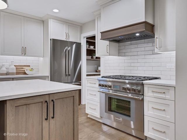 kitchen with white cabinetry, custom range hood, light wood-type flooring, tasteful backsplash, and high end appliances