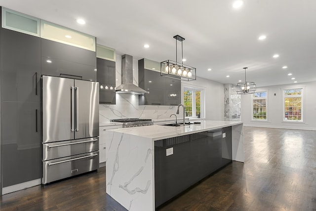 kitchen featuring a kitchen island with sink, hanging light fixtures, high quality fridge, wall chimney exhaust hood, and sink