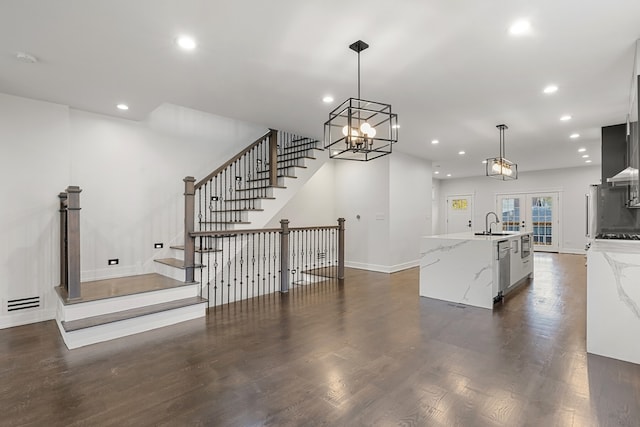 kitchen with light stone countertops, hanging light fixtures, a notable chandelier, a kitchen island with sink, and sink