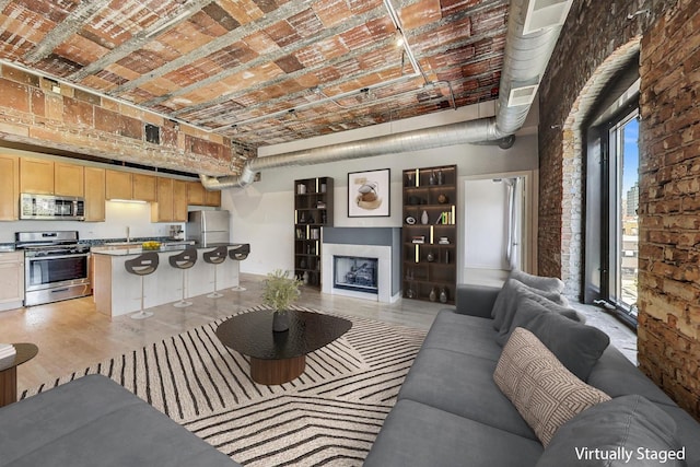 living room featuring a high ceiling, brick wall, brick ceiling, and sink