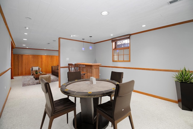 carpeted dining area with wood walls, ornamental molding, and bar