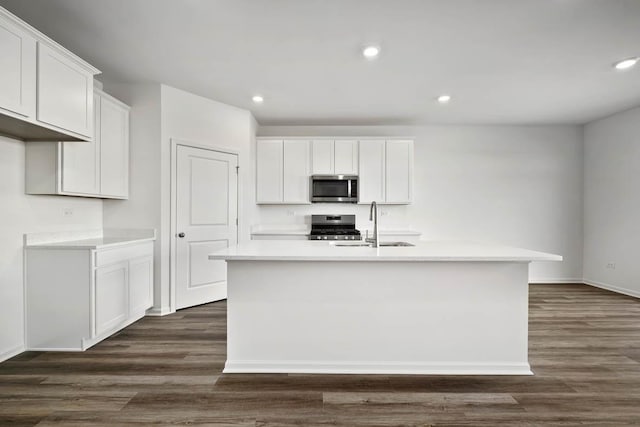 kitchen with appliances with stainless steel finishes, an island with sink, white cabinetry, and dark hardwood / wood-style floors