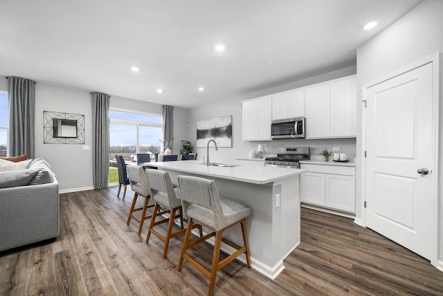 kitchen featuring stainless steel appliances, sink, white cabinetry, dark hardwood / wood-style floors, and a center island with sink