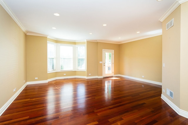 empty room featuring ornamental molding, wood finished floors, visible vents, and baseboards