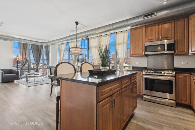 kitchen featuring decorative light fixtures, light hardwood / wood-style floors, a kitchen bar, a kitchen island, and appliances with stainless steel finishes