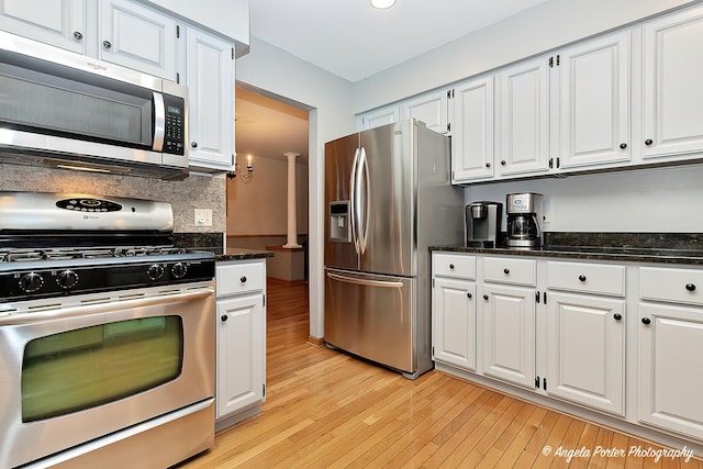 kitchen with stainless steel appliances, light hardwood / wood-style floors, dark stone counters, and white cabinets