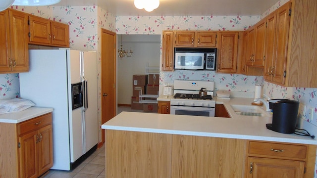 kitchen with a peninsula, white appliances, a sink, light countertops, and wallpapered walls