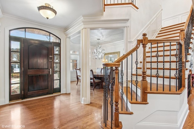 foyer featuring crown molding, wood-type flooring, and a notable chandelier