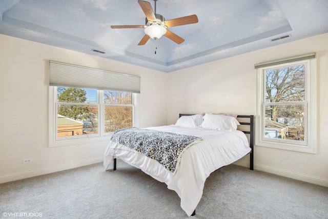 carpeted bedroom with ceiling fan and a tray ceiling