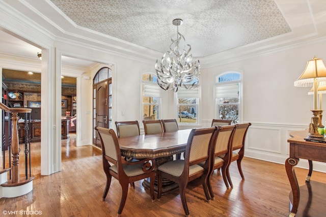 dining space featuring light hardwood / wood-style floors, a tray ceiling, a chandelier, a textured ceiling, and ornamental molding