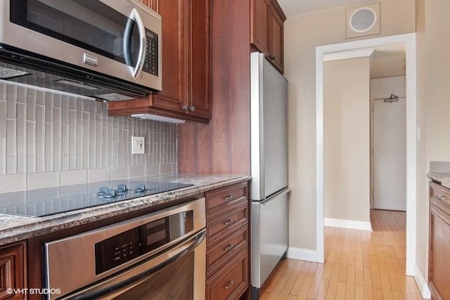 kitchen featuring light stone counters, stainless steel appliances, light hardwood / wood-style floors, and backsplash