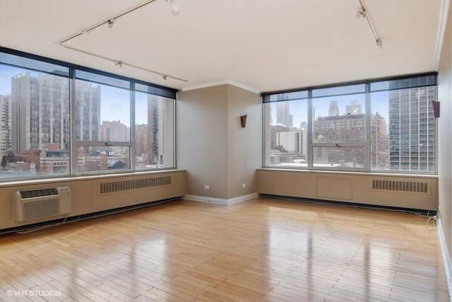 spare room with light wood-type flooring, track lighting, an AC wall unit, and a healthy amount of sunlight