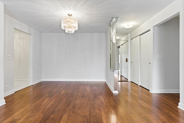 spare room with an inviting chandelier and dark wood-type flooring