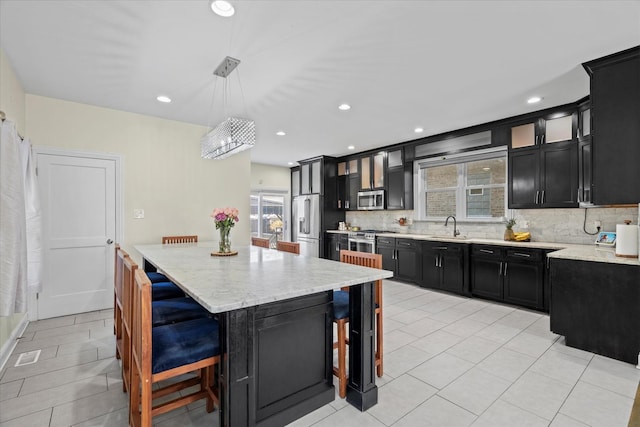 kitchen featuring light stone countertops, appliances with stainless steel finishes, a center island, sink, and hanging light fixtures