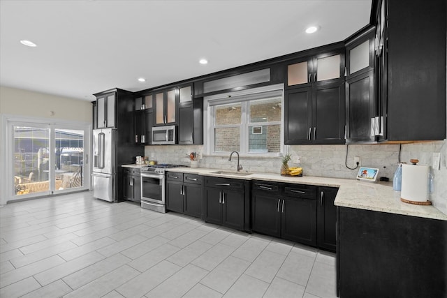 kitchen with sink, stainless steel appliances, light stone counters, and decorative backsplash