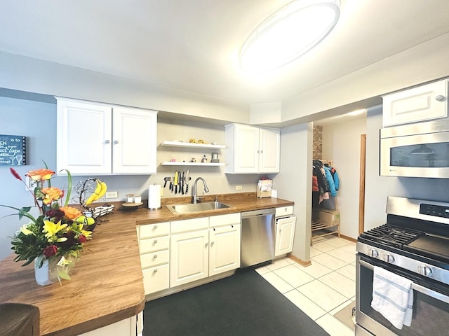 kitchen featuring stainless steel appliances, light tile patterned floors, butcher block countertops, white cabinets, and sink