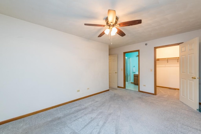 unfurnished bedroom featuring a walk in closet, connected bathroom, a closet, ceiling fan, and light colored carpet