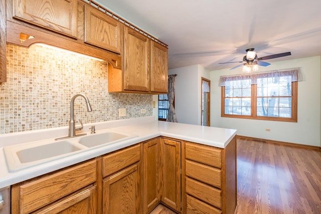 kitchen with sink, backsplash, kitchen peninsula, light wood-type flooring, and ceiling fan