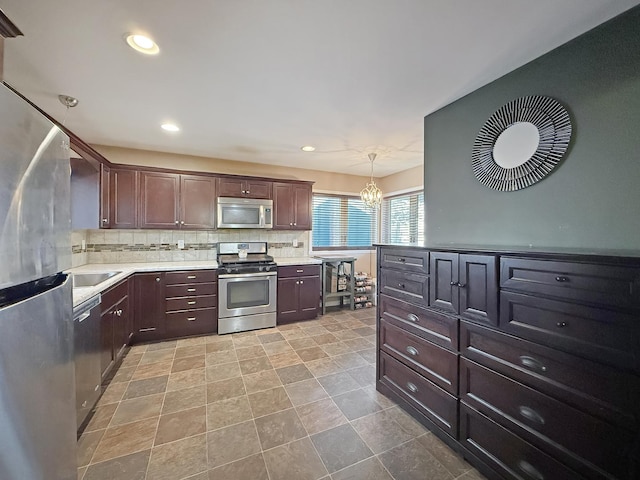 kitchen with a chandelier, appliances with stainless steel finishes, hanging light fixtures, dark brown cabinetry, and tasteful backsplash