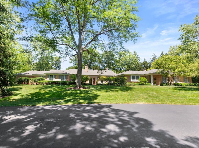 ranch-style house featuring brick siding, a chimney, and a front lawn