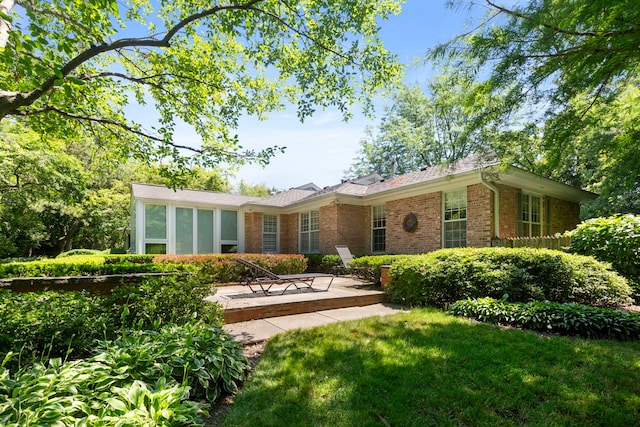 back of property with brick siding, a lawn, and a sunroom