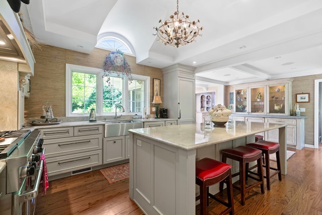 kitchen with a kitchen bar, range with two ovens, light stone counters, wood finished floors, and a sink