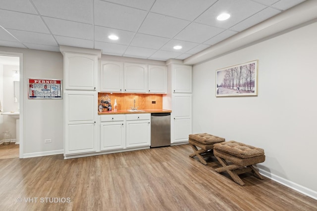 kitchen featuring a paneled ceiling, stainless steel dishwasher, white cabinets, and light wood-type flooring