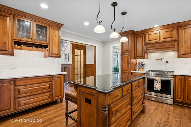 kitchen with wood-type flooring, hanging light fixtures, a kitchen island, and stainless steel gas stove