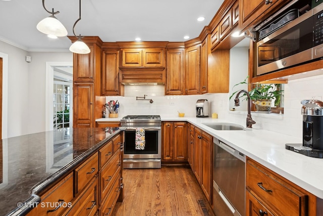 kitchen with sink, dark stone countertops, hanging light fixtures, light hardwood / wood-style floors, and stainless steel appliances