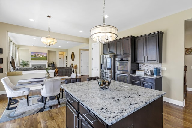 kitchen featuring dark hardwood / wood-style floors, decorative light fixtures, stainless steel appliances, a kitchen island, and backsplash