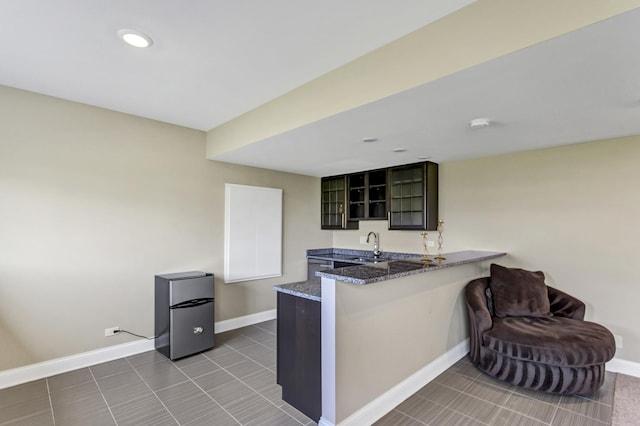 kitchen with kitchen peninsula, stainless steel fridge, dark tile patterned flooring, dark stone countertops, and sink