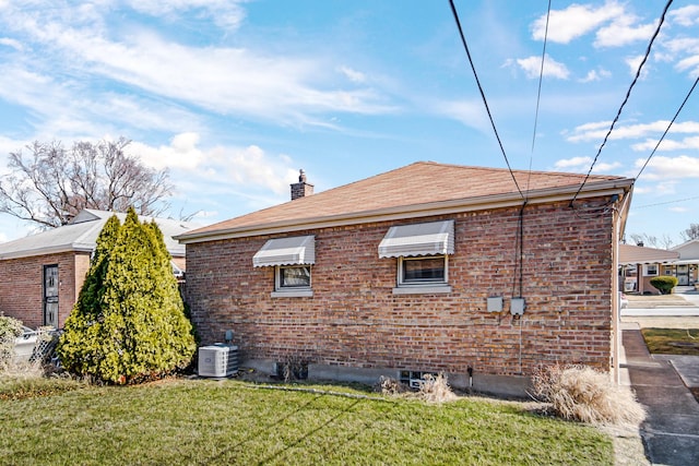 view of side of property with a yard, central AC unit, brick siding, and a chimney