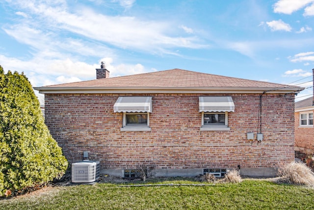 view of home's exterior with brick siding, central AC unit, a chimney, and a lawn