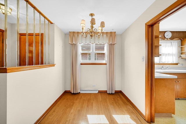 unfurnished dining area with light wood-style flooring, a sink, a baseboard heating unit, an inviting chandelier, and baseboards