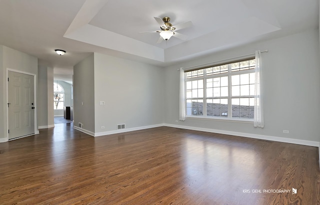 empty room with ceiling fan, dark hardwood / wood-style floors, and a tray ceiling