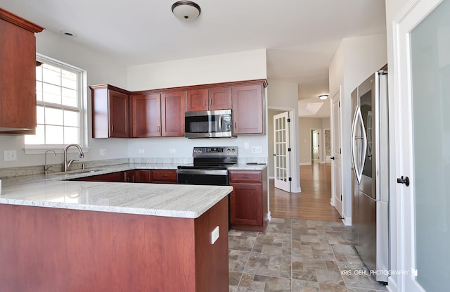 kitchen featuring stainless steel appliances, sink, light stone countertops, and kitchen peninsula