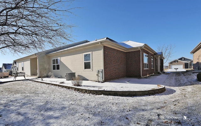 snow covered rear of property featuring a garage and central AC