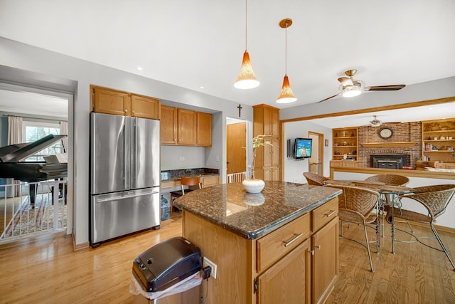 kitchen with pendant lighting, dark stone countertops, stainless steel fridge, a center island, and light hardwood / wood-style floors