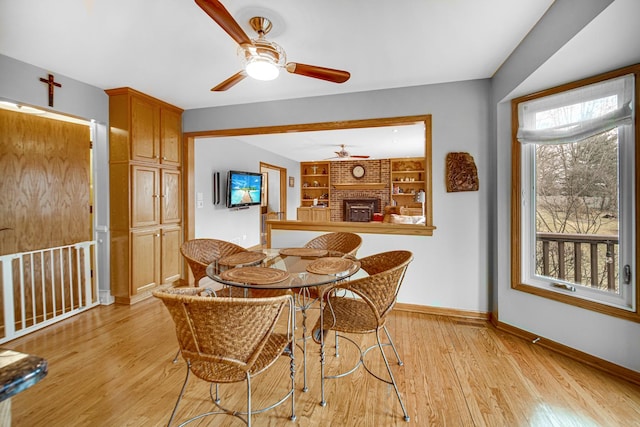 dining area featuring a brick fireplace, built in shelves, ceiling fan, and light wood-type flooring