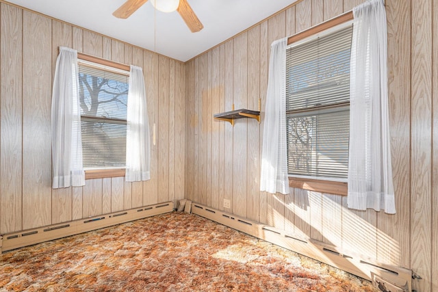 unfurnished room with carpet floors, wooden walls, ceiling fan, and baseboard heating